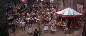 Movie still from “Oliver!” (1968), directed by Carol Reed – A group of people dressed in costumes on a street; Extreme Wide shot, High angle