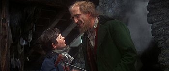 Movie still from “Oliver!” (1968), directed by Carol Reed – A young boy and an old man talking to each other; Medium shot, Over the shoulder angle