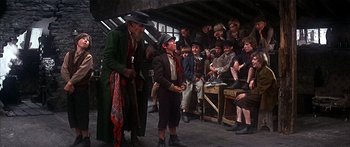 Movie still from “Oliver!” (1968), directed by Carol Reed – A group of people gathered around a man wearing a hat; Wide shot, Low angle