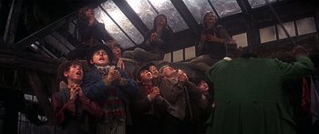 Movie still from “Oliver!” (1968), directed by Carol Reed – A group of young people sitting in a room with their hands clasped together; Medium shot, Low angle