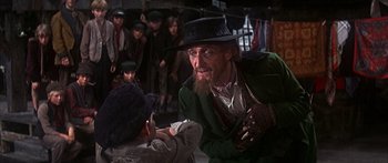 Movie still from “Oliver!” (1968), directed by Carol Reed – A group of people standing next to each other in a room; Medium shot, Over the shoulder angle