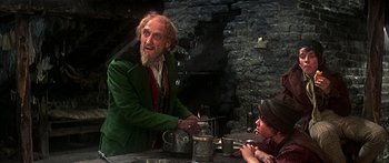 Movie still from “Oliver!” (1968), directed by Carol Reed – An old man in a green jacket is talking to a young boy; Medium shot, Over the shoulder angle