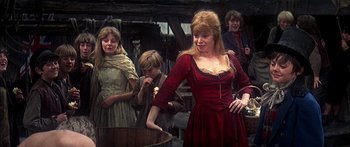 Movie still from “Oliver!” (1968), directed by Carol Reed – A group of people standing around each other in a room; Medium shot, Over the shoulder angle