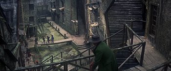Movie still from “Oliver!” (1968), directed by Carol Reed – An old man in a green coat and a hat is standing on some steps; Extreme Wide shot, High angle