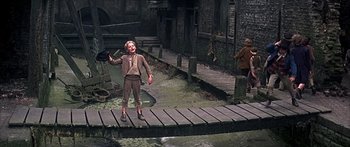Movie still from “Oliver!” (1968), directed by Carol Reed – A man standing on a bridge holding a baseball glove; Wide shot, High angle