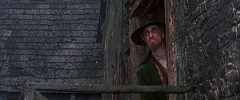 Movie still from “Oliver!” (1968), directed by Carol Reed – A man with a beard wearing a hat looking out of a window; Medium shot, Low angle