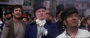 Movie still from “Oliver!” (1968), directed by Carol Reed – A man in a top hat and a blue jacket; Medium shot, Low angle