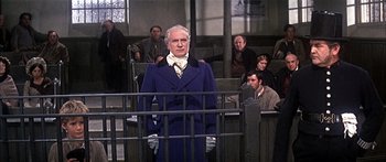 Movie still from “Oliver!” (1968), directed by Carol Reed – An old man in a blue coat standing in front of a fence; Medium shot, Low angle