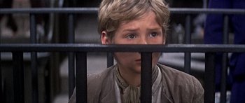 Movie still from “Oliver!” (1968), directed by Carol Reed – A young boy behind a fence looking at the camera; Close Up shot, High angle