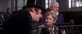 Movie still from “Oliver!” (1968), directed by Carol Reed – A man in a top hat talking to a young boy; Medium shot, Over the shoulder angle