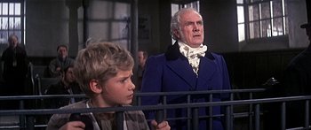 Movie still from “Oliver!” (1968), directed by Carol Reed – A young boy and an older man in a blue suit; Medium shot, Low angle