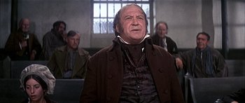 Movie still from “Oliver!” (1968), directed by Carol Reed – An older man in a brown coat and a white shirt; Medium shot, Low angle
