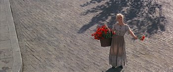 Movie still from “Oliver!” (1968), directed by Carol Reed – A woman holding a basket full of red flowers; Wide shot, High angle