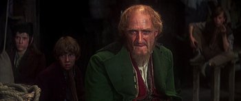 Movie still from “Oliver!” (1968), directed by Carol Reed – An old man with a beard and long hair and wearing a green jacket; Close Up shot, Over the shoulder angle