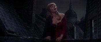 Movie still from “Oliver!” (1968), directed by Carol Reed – A woman in a red dress singing in front of a dark background; Medium shot, Low angle