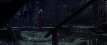 Movie still from “Oliver!” (1968), directed by Carol Reed – A woman in a red dress standing on the side of a building; Wide shot, High angle