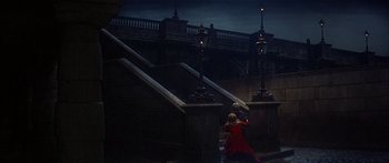 Movie still from “Oliver!” (1968), directed by Carol Reed – A woman in a long red coat standing on a set of stairs; Extreme Wide shot, High angle
