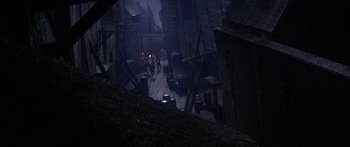 Movie still from “Oliver!” (1968), directed by Carol Reed – People are walking down a dark alley in a city; Extreme Wide shot, High angle