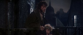 Movie still from “Oliver!” (1968), directed by Carol Reed – A man and a boy sitting next to each other on a ledge; Medium shot, Low angle