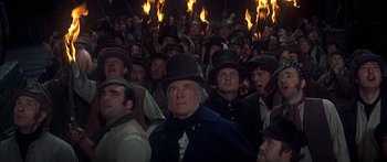 Movie still from “Oliver!” (1968), directed by Carol Reed – A group of people wearing hats in front of a crowd; Medium shot, High angle