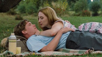 Movie still from “On Chesil Beach” (2017), directed by Dominic Cooke – A man and a woman laying on a blanket in the grass; Medium shot, High angle