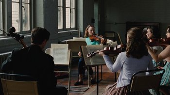 Movie still from “On Chesil Beach” (2017), directed by Dominic Cooke – A group of people sitting in a room playing musical instruments; Wide shot, Over the shoulder angle