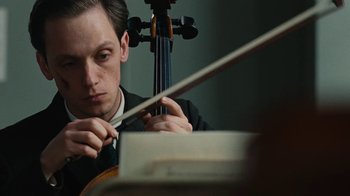 Movie still from “On Chesil Beach” (2017), directed by Dominic Cooke – A man in a suit and tie playing the violin; Close Up shot, Low angle