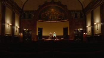 Movie still from “On Chesil Beach” (2017), directed by Dominic Cooke – Two people standing in front of a large painting in an auditorium; Extreme Wide shot, Low angle