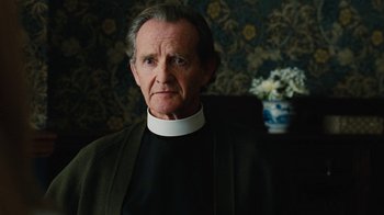 Movie still from “On Chesil Beach” (2017), directed by Dominic Cooke – An older man wearing a priest's collar; Close Up shot, Low angle