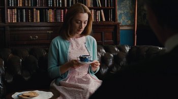 Movie still from “On Chesil Beach” (2017), directed by Dominic Cooke – A woman sitting on a couch holding a tea cup; Medium shot, Over the shoulder angle