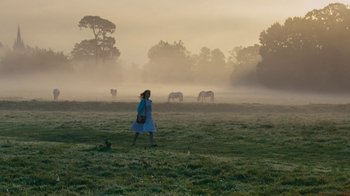 Movie still from “On Chesil Beach” (2017), directed by Dominic Cooke – A woman in a blue dress walking across a grass field; Wide shot, Low angle