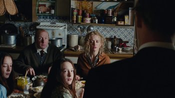 Movie still from “On Chesil Beach” (2017), directed by Dominic Cooke – A group of people sitting at a table in a kitchen; Medium shot, Over the shoulder angle