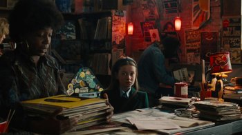 Movie still from “On Chesil Beach” (2017), directed by Dominic Cooke – A young girl sitting at a table in front of stacks of papers; Medium shot, Over the shoulder angle