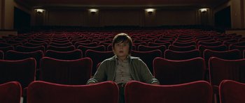 Movie still from “Mr. Nobody” (2009), directed by Jaco Van Dormael – A person sitting in a red chair in an empty theater; Wide shot, High angle