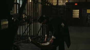 Movie still from “Once Upon a Time in America” (1984), directed by Sergio Leone – A man in a black suit and a black hat looking into a box; Wide shot, High angle