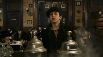 Movie still from “Once Upon a Time in America” (1984), directed by Sergio Leone – A young man in a hat and a black jacket stands next to two silver bells; Medium shot, Low angle