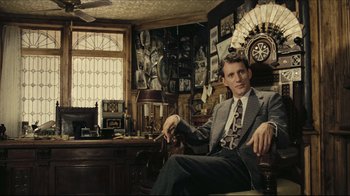 Movie still from “Once Upon a Time in America” (1984), directed by Sergio Leone – A man in a suit and tie sitting in front of a desk; Medium shot, Low angle