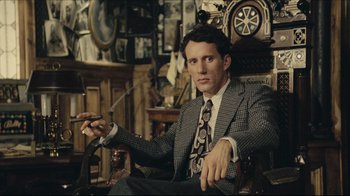 Movie still from “Once Upon a Time in America” (1984), directed by Sergio Leone – A man in a suit and tie sitting in a chair; Medium shot, Low angle