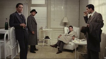 Movie still from “Once Upon a Time in America” (1984), directed by Sergio Leone – A man in a coat and hat sitting in a chair in front of two other men; Wide shot, High angle