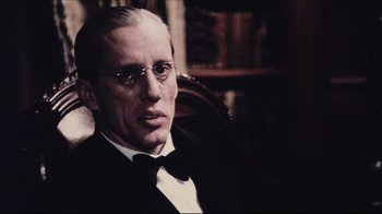Movie still from “Once Upon a Time in America” (1984), directed by Sergio Leone – A man in a suit sitting in a chair in front of a book case; Close Up shot, Low angle