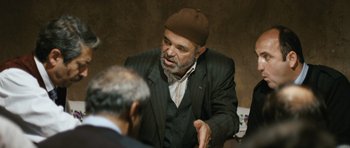 Movie still from “Once Upon a Time in Anatolia” (2011), directed by Nuri Bilge Ceylan – A man wearing a hat talking to another man in a suit; Medium shot, Over the shoulder angle