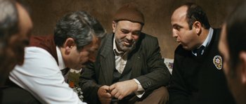 Movie still from “Once Upon a Time in Anatolia” (2011), directed by Nuri Bilge Ceylan – A man in a suit and a hat sitting on the ground; Medium shot, Over the shoulder angle