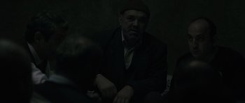 Movie still from “Once Upon a Time in Anatolia” (2011), directed by Nuri Bilge Ceylan – A man sitting in a dark room wearing a hat; Medium shot, Over the shoulder angle