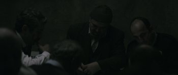 Movie still from “Once Upon a Time in Anatolia” (2011), directed by Nuri Bilge Ceylan – A man in a suit and a hat is looking down at his tie; Medium shot, Over the shoulder angle