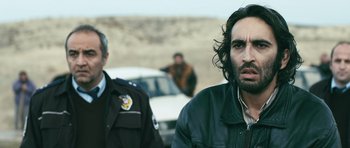 Movie still from “Once Upon a Time in Anatolia” (2011), directed by Nuri Bilge Ceylan – A man in a leather jacket standing next to another man in front of a white car; Close Up shot, Over the shoulder angle