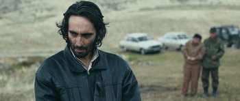 Movie still from “Once Upon a Time in Anatolia” (2011), directed by Nuri Bilge Ceylan – A man in a black jacket standing next to two cars; Close Up shot, Over the shoulder angle