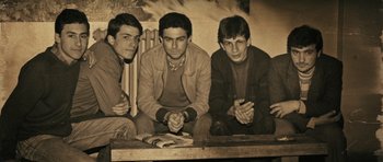 Movie still from “Once Upon a Time in Anatolia” (2011), directed by Nuri Bilge Ceylan – Three young men sitting on the ground with their hands clasped together; Medium shot, Low angle