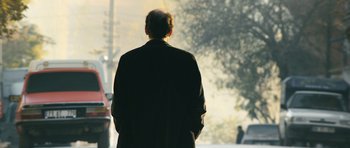 Movie still from “Once Upon a Time in Anatolia” (2011), directed by Nuri Bilge Ceylan – A man in a suit is standing on the sidewalk; Medium shot, Over the shoulder angle