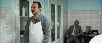 Movie still from “Once Upon a Time in Anatolia” (2011), directed by Nuri Bilge Ceylan – A man with a white apron standing next to another man in a suit; Medium shot, Over the shoulder angle