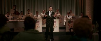 Movie still from “One Night in Miami...” (2020), directed by Regina King – A man standing in front of a group of people; Medium shot, Over the shoulder angle